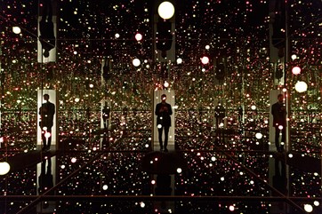 Man standing in a dark mirrored room filled with numerous small lights.