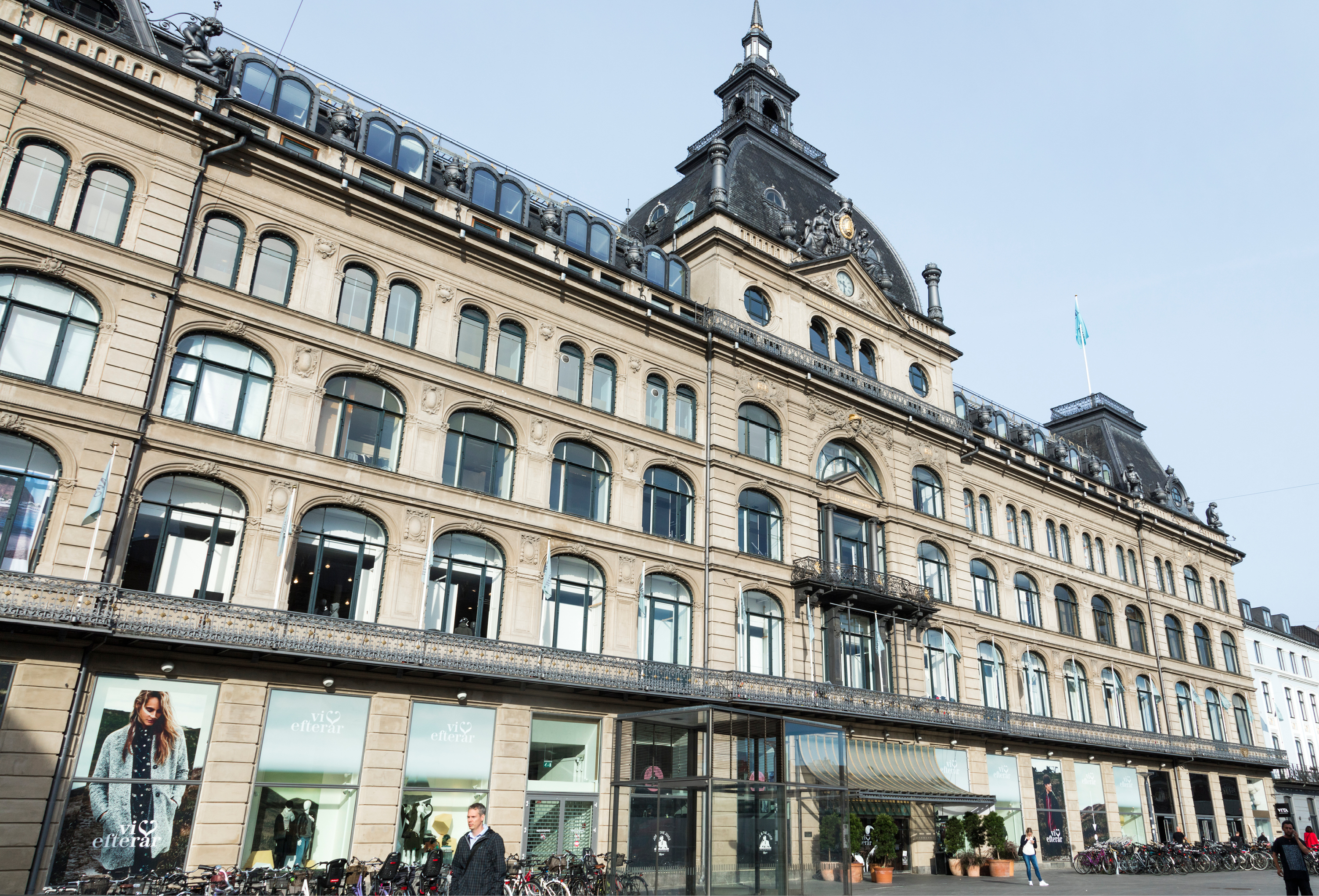 Modern photo of Magasin du Nord in Copenhagen today, featuring the restored facade and contemporary window displays blending tradition with modern style.