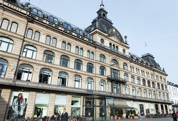 Modern photo of Magasin du Nord in Copenhagen today, featuring the restored facade and contemporary window displays blending tradition with modern style.