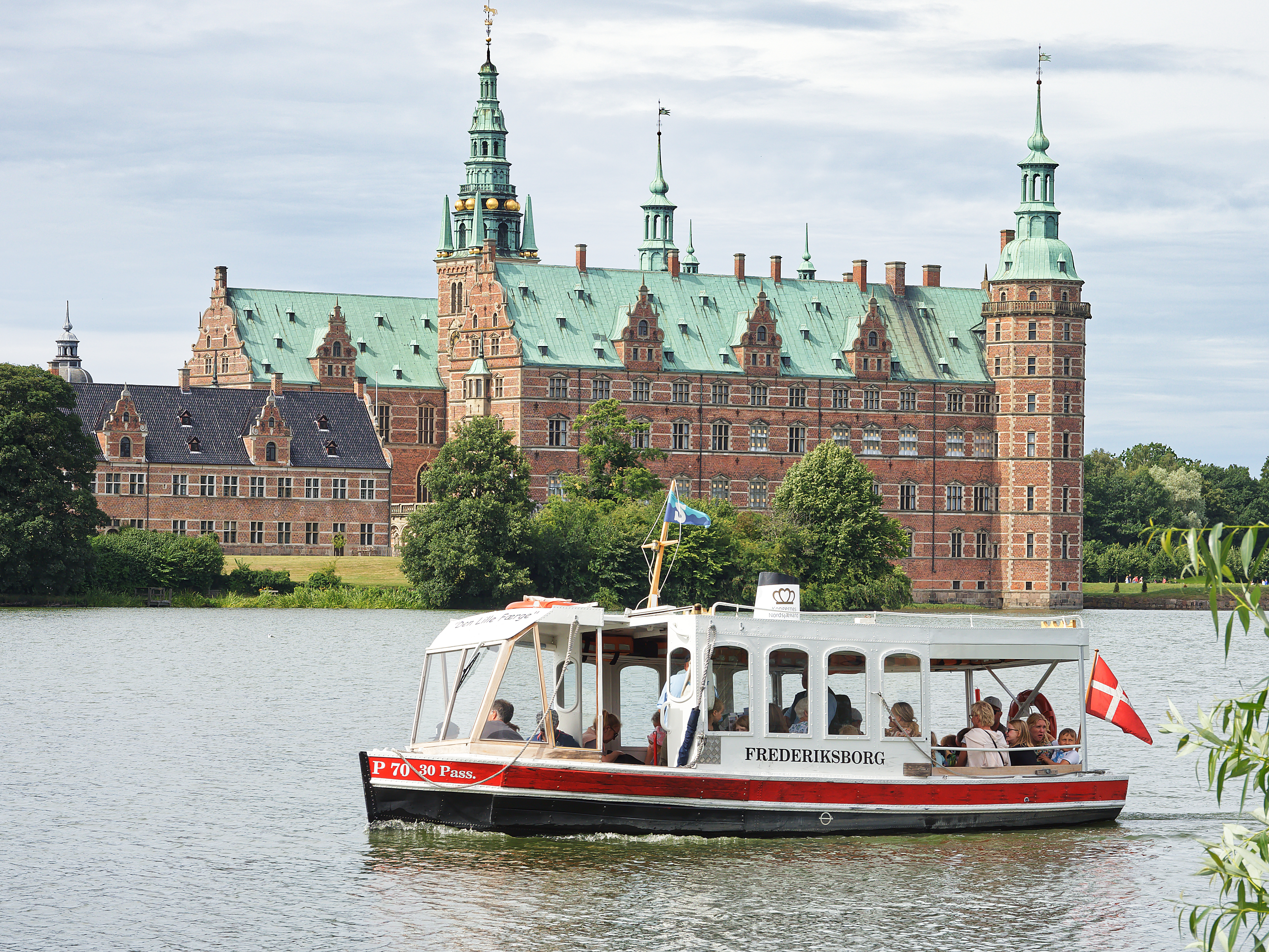 Frederiksborg Castle viewed across the water with a tour boat passing in the foreground.